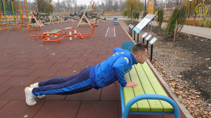 Хлопець робить вправу з віджимань на лаві на вуличному спортивному майданчику