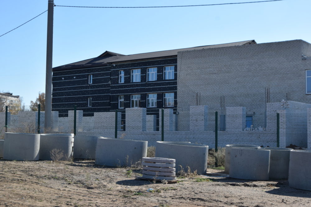 Частково вигнана прибудова до основної будівлі школи, на передньому плані, бетонні  труби великого діаметра.