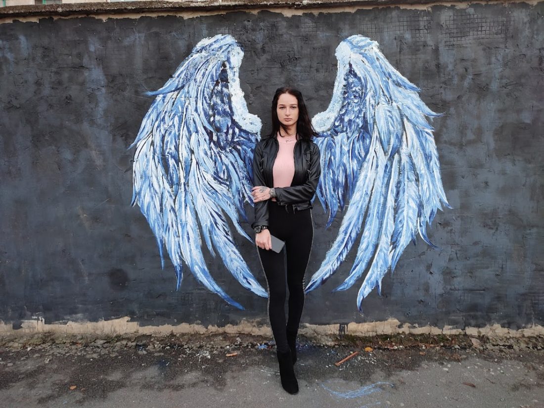 Малюнок на стіні у вигляді блакитних крил. На передньому плані стоїть дівчина, утворюючи з ними єдиний образ.