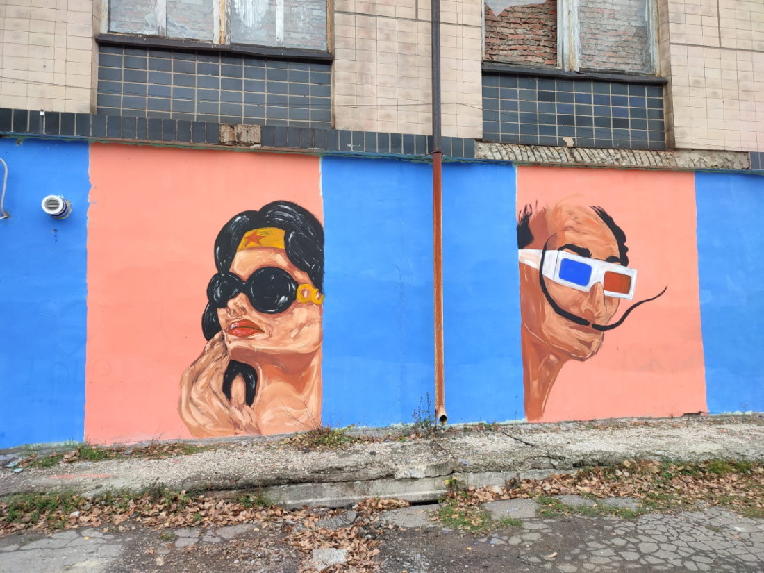 Портрети на стіні. Персонаж коміксів Woder women у темних окулярах та Сальвадор Далі в окулярах із синім і червоним скельцями.
