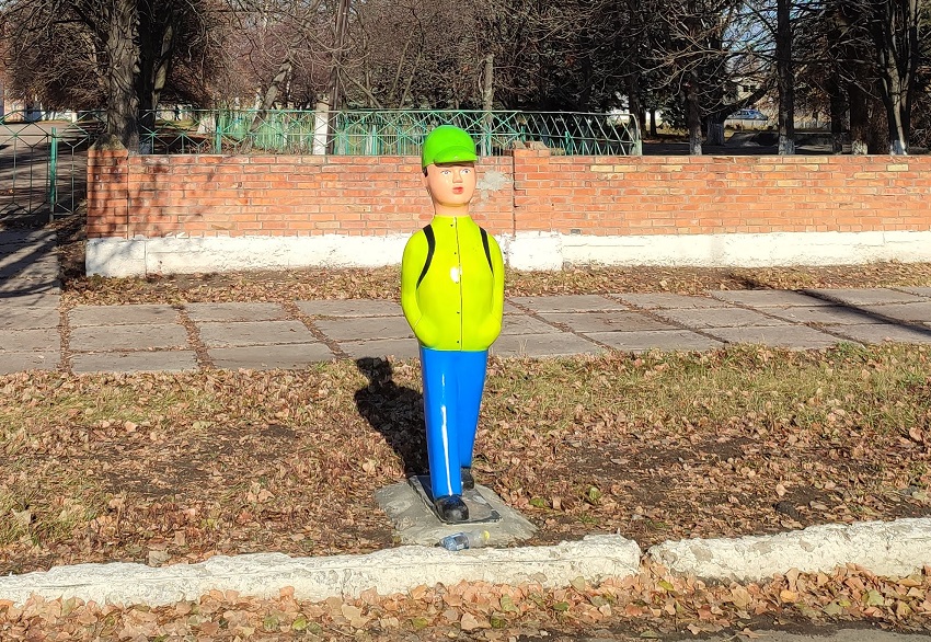 Фігурка школяра у яскравій куртці біля дороги. На задньому плані – будівля школи.
