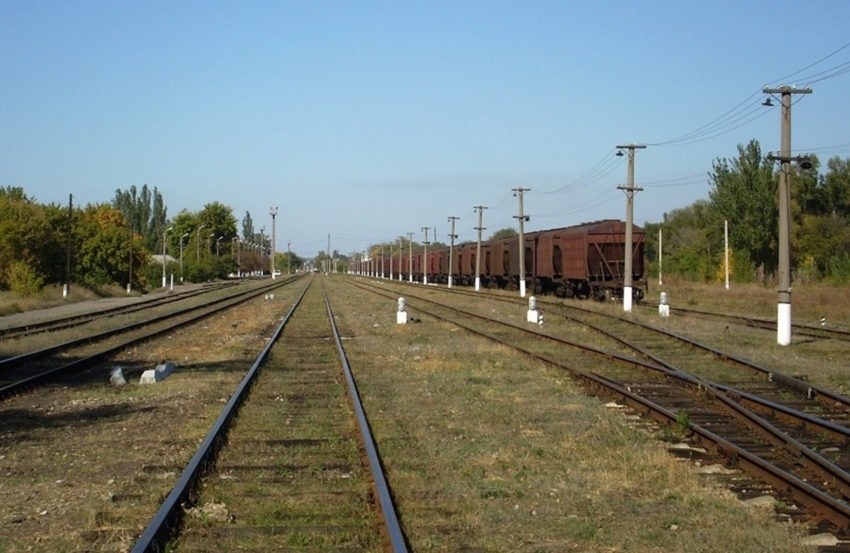 На передньому плані шість залізничних колій, які прямують за горизонт. На одній з них – у правій частині знімка – товарні вагони