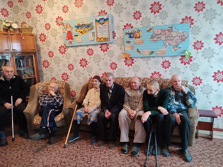 Семеро літніх людей та людей з видимими ознаками інвалідності сидять у кріслах та на дивані