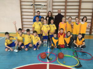 Група дітей у спортивній формі та зі спортивним інвентарем позує для фото з якимись трьома дорослими