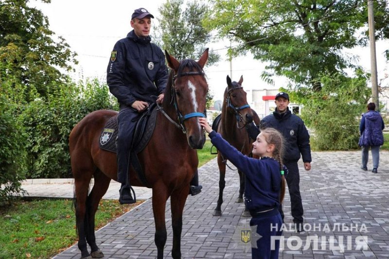 Поліцейський верхи на коні. Дівчинка гладить морду тварини.