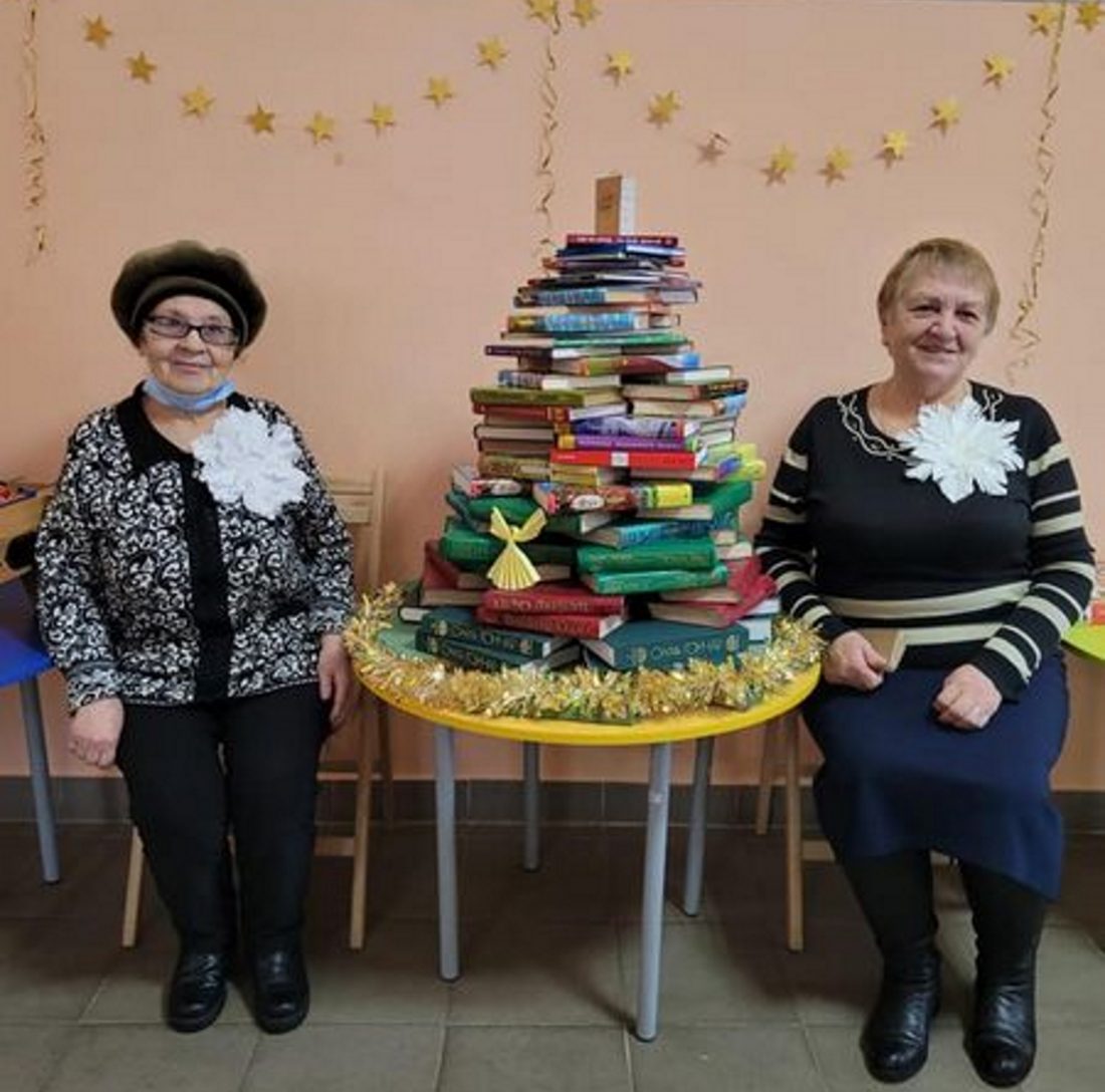 Дві літні жінки позують біля інсталяції з книжок