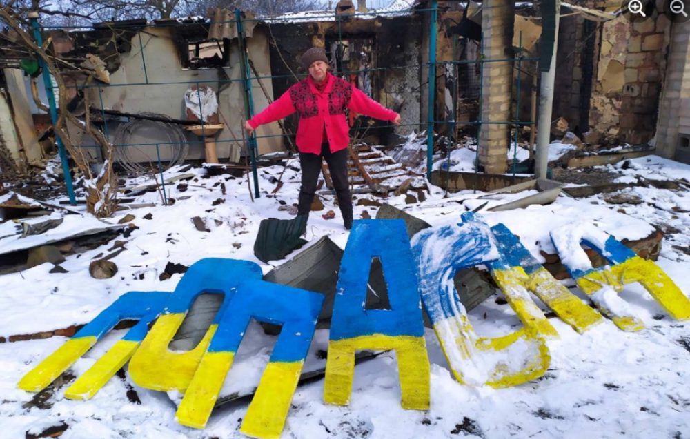 Ірина Крамаренко з назвою рідного міста на фоні руїн свого дому